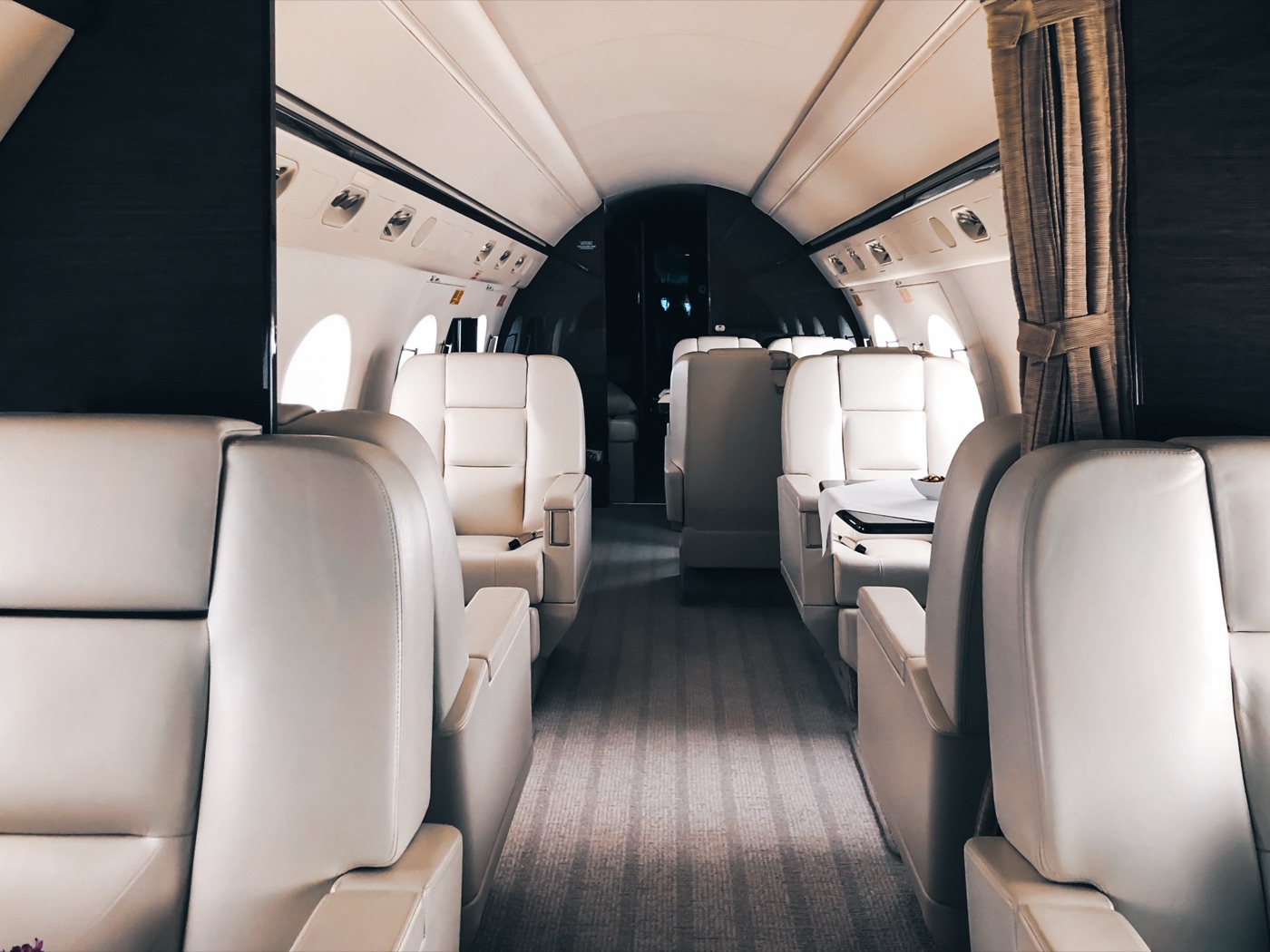 An empty business-jet cabin with cream seats and a central aisle.