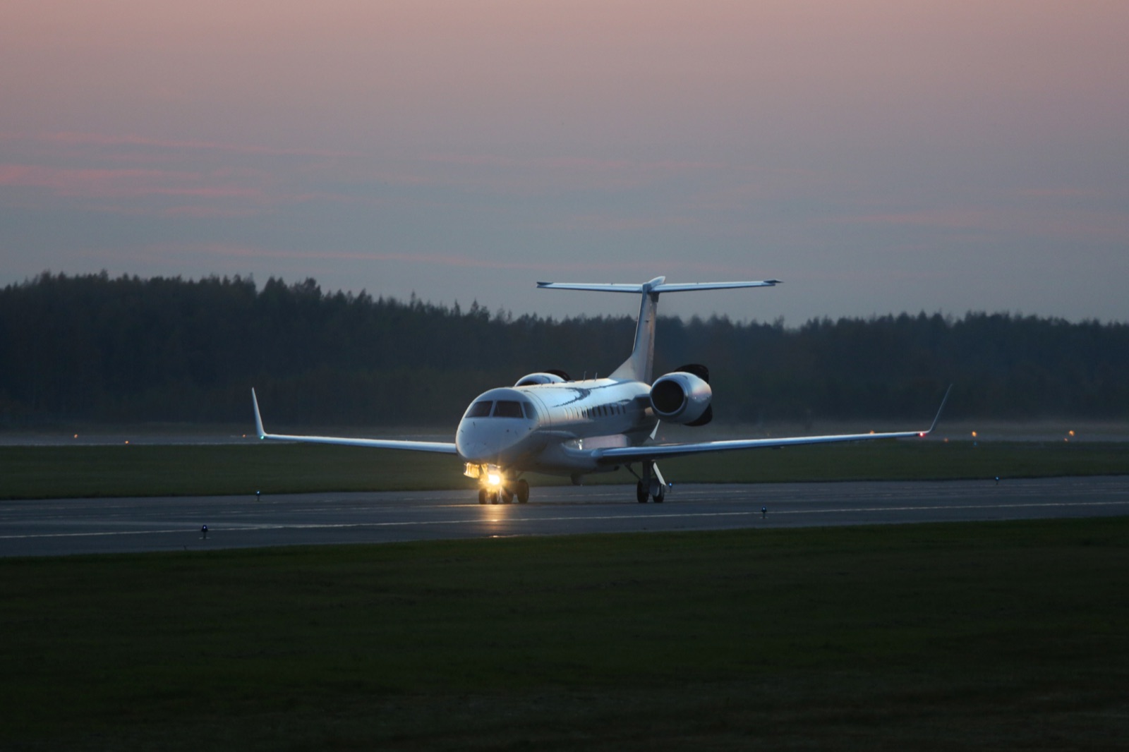 A business jet taxiing at dusk with its lights illuminated.