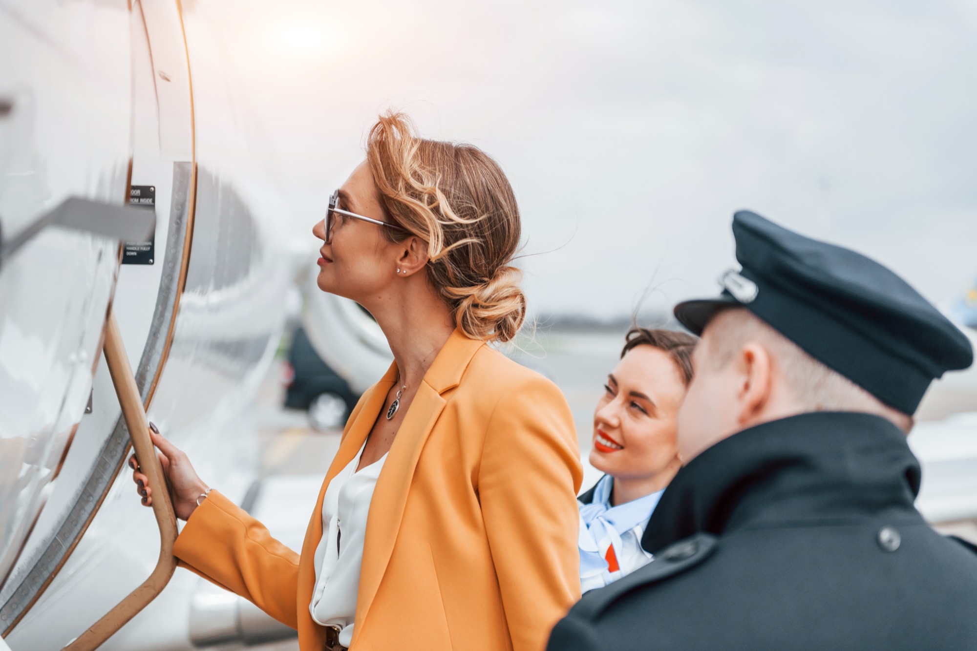A customer boarding a business jet with a pilot and cabin crew beside her.